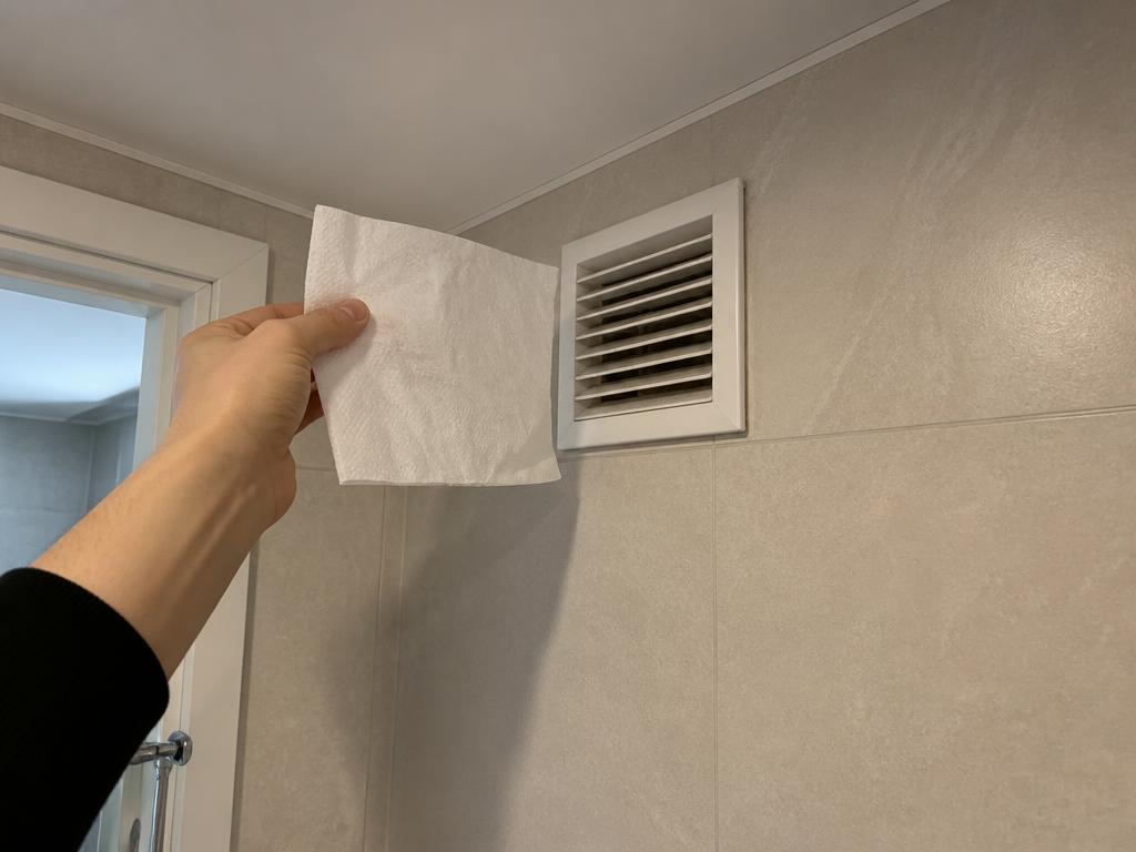 Vannitoa seinal olev ventilatsioonivõre, mille juures kontrollitakse paberitükiga õhutõmmet
